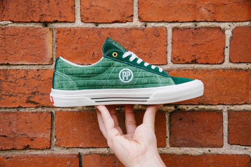 hand holding a green vans shoes, white sole, brick wall ,